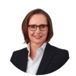 Frau mit braunen Haaren und Brille in Anzug.